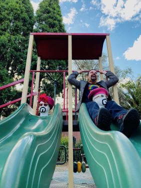 Jeremy Moses sits atop a playground slide with two foam heads dressed as his alter-egos.